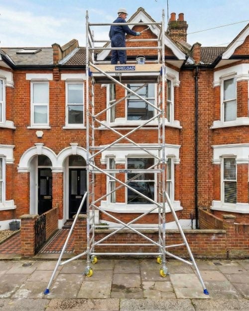 Worker on a two-storey industrial scaffold tower positioned against a residential building for exterior access