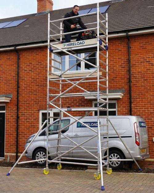 Scaffold tower hire London with worker on elevated platform accessing residential roof and gutters