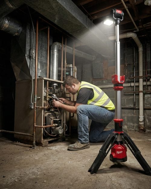 Technician using Milwaukee M12 cordless tripod stand light while servicing boiler in dark basement - LED Tripod Site Work Light