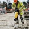 Heavy Duty Road Breaker Hire London | Electric Jackhammer for Concrete and Asphalt 19 Worker using heavy duty electric road breaker to break asphalt on London roadworks site with construction crew in background