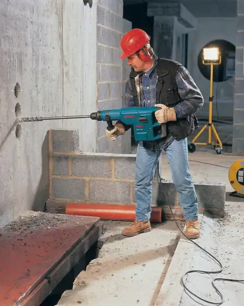 Rotary Hammer Hire London | Bosch GBH 11 DE SDS Max Combi Hammer (11kg) 14 Construction worker drilling into concrete wall with Bosch SDS Max rotary hammer hire on active building site with safety board