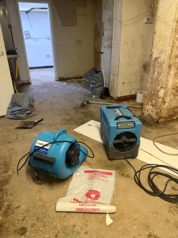 Dehumidifier and air mover drying a water-damaged floor after a leak